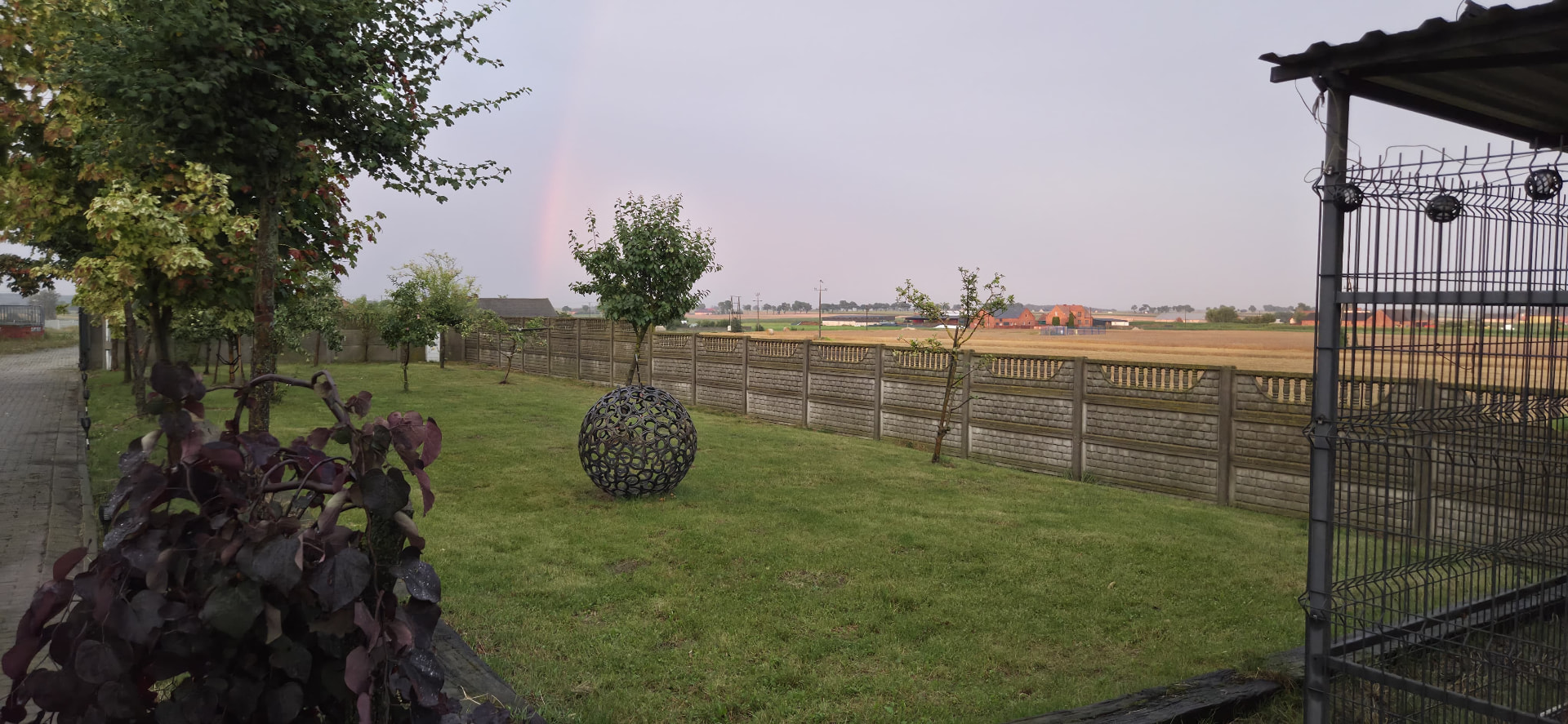 Ogród z kulą z podków i tęczą nad polami po deszczu
